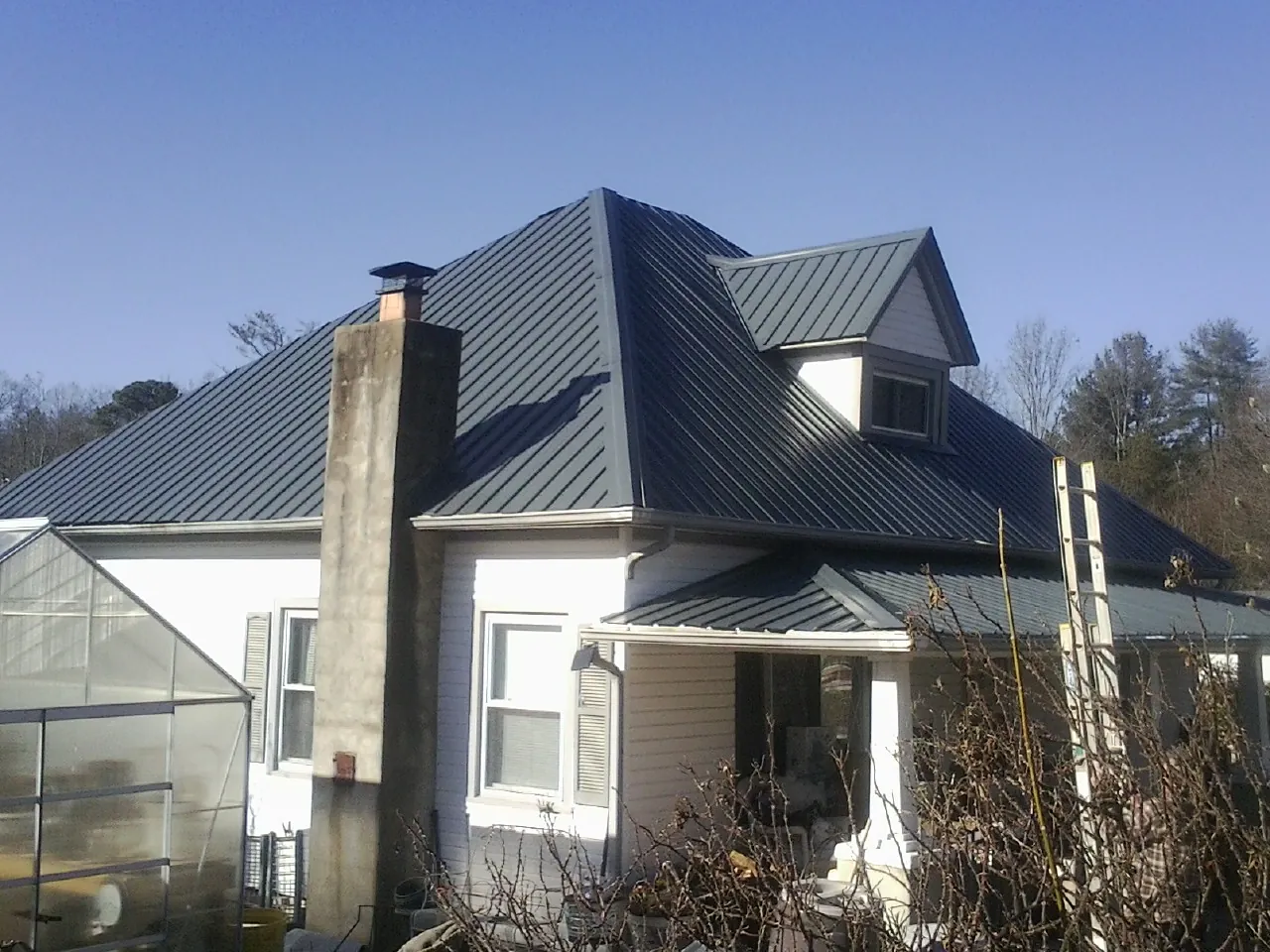 Dark blue standing seam metal roof on a white farmhouse with dormer — Slate & Tile Roof Repair by Roofing Brothers in Divernon