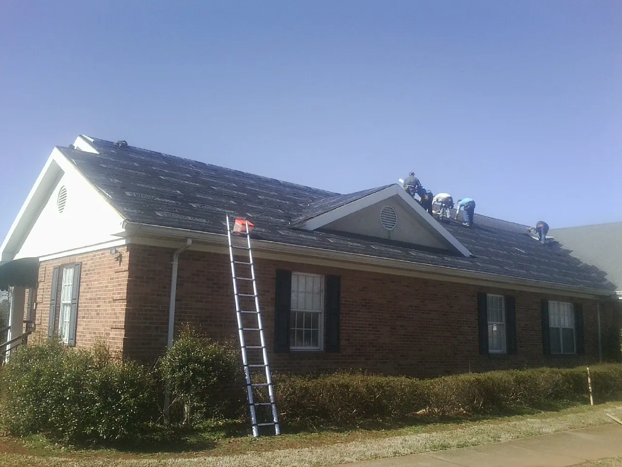Crew tearing shingles off a brick ranch roof with a ladder set — Metal Roof Repair work by our crew in Divernon