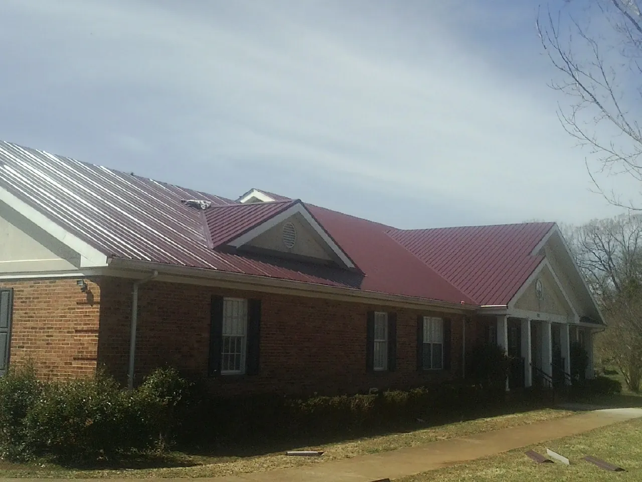 Red metal roof with gabled entries on a long brick building, from a Hail Damage Roof Repair job in Divernon