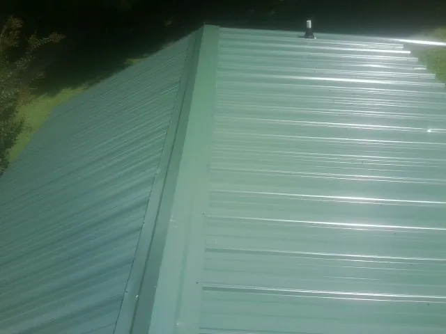 New green metal panels meeting at the ridge of a roof — Flat Roof Repair work by our crew in Divernon