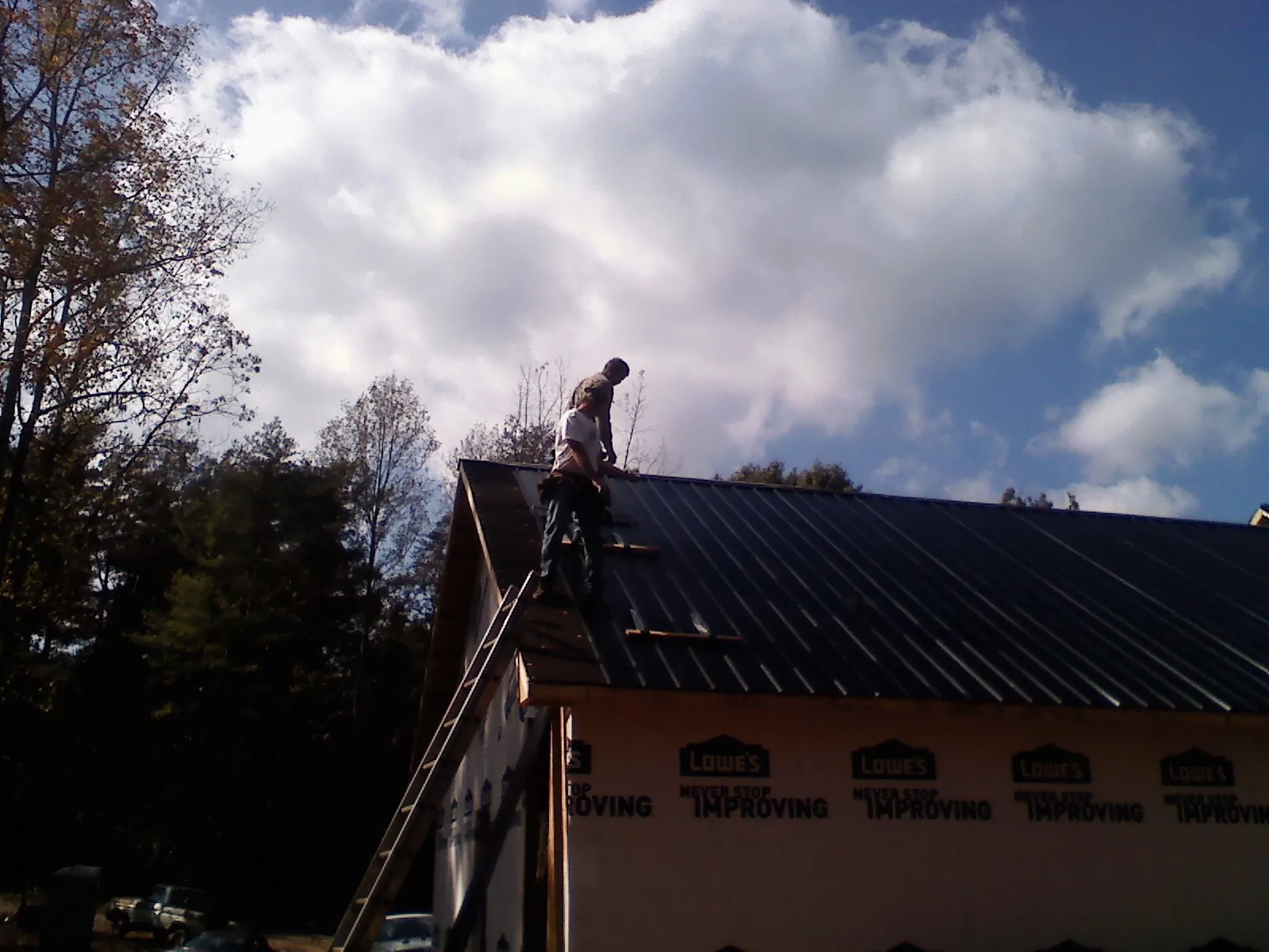 Roofer fastening dark metal panels high against a cloudy sky, from a Roof Inspection job in Divernon
