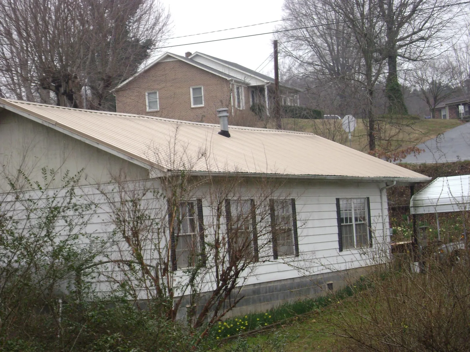 Tan metal roof on a white sided house set into a hillside — Commercial Roofing by Roofing Brothers in Divernon